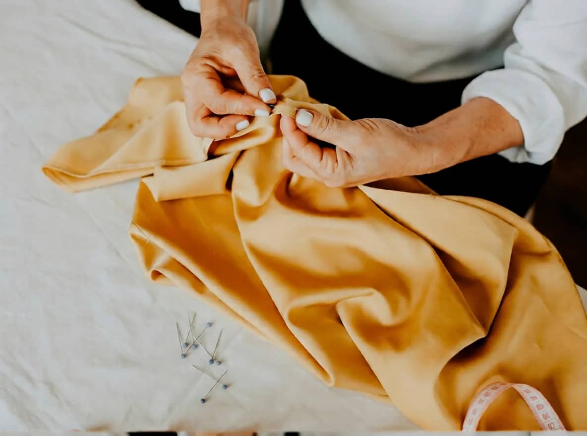 Croitor lucrând la ajustarea unei haine pe masa de lucru